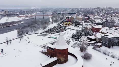 Kaunas-Castle-covered-in-snow-during-snowfall,-aerial-ascending-view