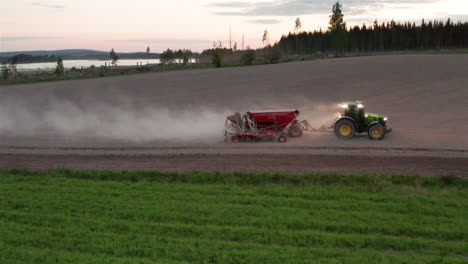AERIAL---Tractor-sowing-seeds-at-dusk,-Hedemora,-Sweden,-wide-shot-backwards