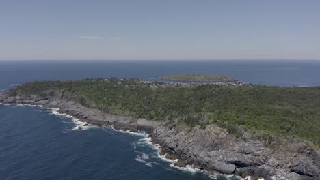 Drone-shot-flying-above-a-small-island-in-Maine-with-a-rocky-coastline-and-the-town-in-the-background
