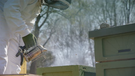 BEEKEEPING---A-beekeeper-smokes-beehives-to-keep-bees-calm,-slowmo-medium-shot