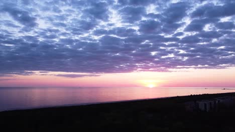 Beautiful-aerial-vibrant-high-contrast-pink-purple-sunset-with-blue-clouds-over-Baltic-sea-at-Liepaja,-distant-ships-in-the-sea,-wide-angle-descending-drone-shot-camera-tilt-up-slow-zoom-in