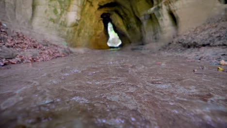 Low-angle-shot-of-natural-stream-flowing-through-cave-during-sunny-day-in-autumn