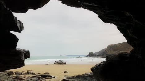 View-Looking-Through-Cave-to-Beach-with-Car-Towing-Water-Ski,-St