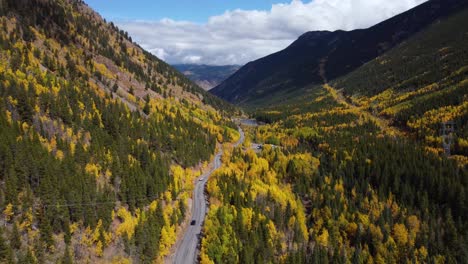 Descending-next-to-Colorado-highway-surrounded-by-golden-aspens-in-the-fall,-Aerial