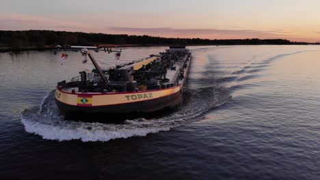 Vista-Frontal-De-Una-Barcaza-Cisterna-Navegando-Por-El-Río-Durante-La-Hora-Dorada-Al-Atardecer-En-Países-Bajos