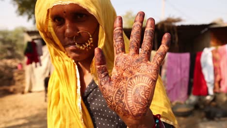 Indian-woman-with-yellow-veil-on-head-showing-palm-of-her-hand-tattooed-with-henna,-Rajasthan