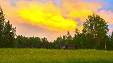 Thermowood-Cabin-in-beautiful-green-landscape-and-forest-in-background---Colorful-flying-clouds-at-sky-during-sunset---5K-Timelapse-shot