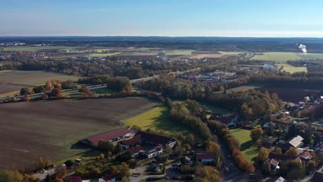 Smooth-backward-flight-over-a-bavarian-town-in-the-fall-season,-idyllic-living-next-to-autumnal-colored-trees-and-fields