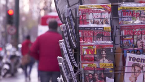 Man-running-past-magazines-at-newspaper-stand-in-the-center-of-Athens,-Greece