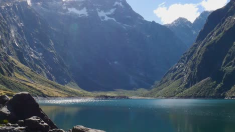 Wide-shot-of-idyllic-Lake-Marian-with-sun-reflection-of-water-surface-surrounded-by-massive-mountains-in-Fiordland-National-Park-during-summer