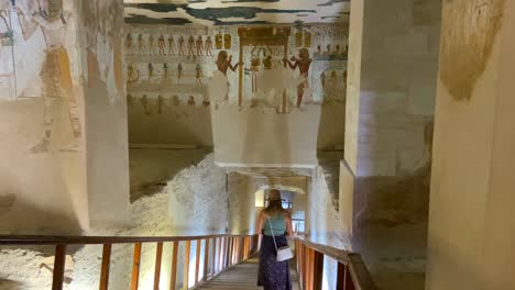 Young-woman-with-a-hat-descending-the-stairs-of-a-sacred-tomb-that-leads-to-a-sarcophagus-decorated-with-paintings-in-the-Valley-of-the-Kings