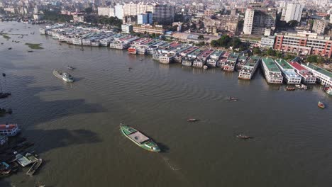 Aerial:-dockyard-at-Buriganga-river-bank-with-city-landscape-in-Dhaka,-Bangladesh---drone-tilt-up-shot