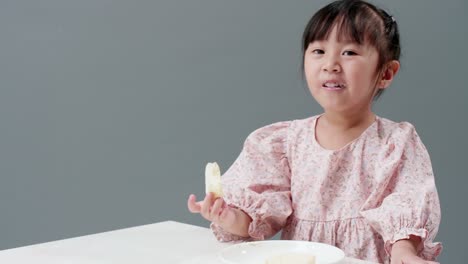 Asiatisches-Kind-Isst-Ein-Stück-Süßigkeiten-Im-Studio-Mit-Grauem-Hintergrund
