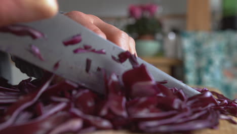 Extreme-close-up-woman's-hand-gently-chopping-in-pieces-Italian-purple-red-cabbage-with-a-rounded-sharp-knife-in-the-kitchen