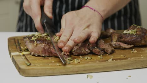 Close-up-on-chef-slicing-freshly-cooked-beef-steak-on-wooden-cut-board