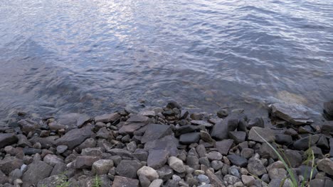Pebbles-and-rocks-along-a-lake-shore-with-wave-washing-on-a-quiet-summer-day