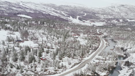 Camino-Rural,-Río-Y-Bosque-De-Coníferas-Cubierto-De-Nieve-Durante-El-Invierno-En-Dovre,-Condado-De-Innlandet,-Noruega---Toma-Aérea-De-Drones