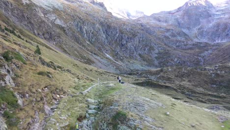 Two-hikers-at-Val-d'Arrouge-ridge-stone-path-leading-to-Lac-d'Espingo-in-Haute-Garonne,-Pyrénées,-France,-Aerial-flyover-approach-shot