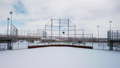 Reveal-of-baseball-and-softball-diamond,-pitchers-mound,-and-dugouts-with-freshly-fallen-snow,-aerial