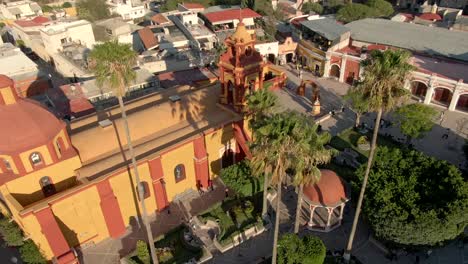 Aerial-View-Of-Saint-Sebastian's-Temple-And-Tourists-In-The-Main-Plaza-Of-Bernal,-Querétaro,-Mexico---drone-shot