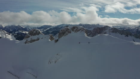 Antena-De-Dos-Esquiadores-En-Una-Ladera-Cubierta-De-Nieve-Con-Un-Hermoso-Paisaje-Montañoso-En-El-Fondo