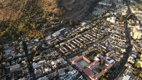 Aerial-dolly-in-of-Santiago-city-neighborhood-buildings-near-San-Cristobal-hillside-at-golden-hour,-Chile