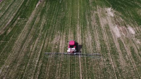 Aerial-view-of-farming-tractor-spraying-on-field-with-sprayer,-herbicides-and-pesticides-insecticide-to-the-green-field-plowed-land-for-a-non-organic-farming