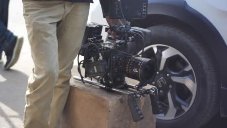 Person-And-Professional-Cinema-Camera-Resting-Beside-Car-Wheel-On-Set-In-Karachi