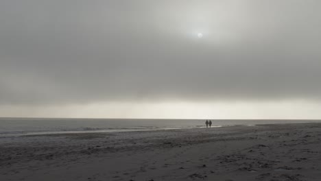 Couple-in-distant-walking-on-a-beach-on-a-foggy-Scandinavian-day-in-slow-motion-and-4K