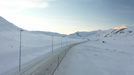 Norwegischer-Winterstraßenübergang-Bei-Eldrevatn-Im-Hemsedal-Gebirge-Zwischen-Ost-Und-West---Überquerung-Der-Luftaufnahme-Bei-Sonnenuntergang-Und-Flug-über-Die-Schneebedeckte-Straße