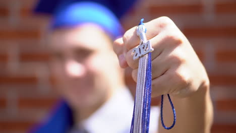Close-up-of-happy-male-graduate-holds-up-his-2021-graduation-tassel