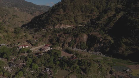 village-on-the-side-of-a-mountain-in-a-remote-community-surrounded-by-trees-jungle-farms-in-valley-Benguet-Philippines-side-trucking-wide-angle-aerial-drone