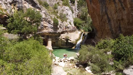 Alquezar-in-Huesca,-Aragon,-Spain-–-Pasarelas-del-Vero-Hike---Aerial-Drone-View-of-Tourists-Hiking-the-Walking-Bridge-and-Swimming-at-the-Waterfall