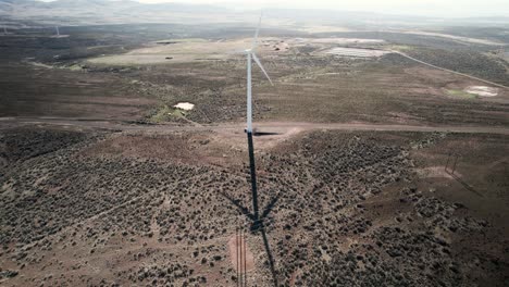 Long-shadows-from-a-tall-wind-powered-electric-generator,-green-renewable-sustainable-electricity,-aerial-orbit