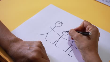 Crop-View-Of-Person-Drawing-Stick-Figures-Of-A-Family-On-White-Bond-Paper