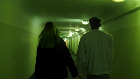 Refugee-couple-walking-inside-the-corridor-of-a-concrete-bunker-serving-as-a-bomb-shelter,-back-view