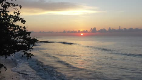 Luftdrohne-Fliegt-über-Einen-Kokosnussbaum-Am-Strand-Mit-Wellen,-Die-Während-Des-Sonnenaufgangs-In-Bali,-Indonesien,-Zusammenbrechen