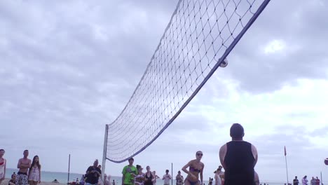 Team-of-volleyball-players-passing-ball-and-scoring-point-during-beach-side-volley-ball-competition-filmed-with-wide-angle-in-slow-motion