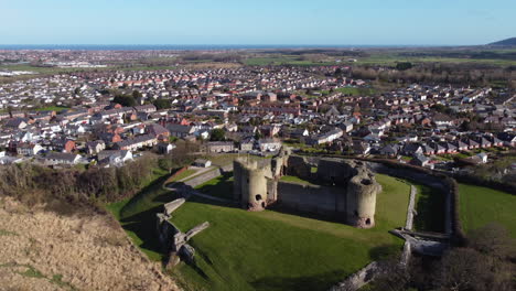 An-aerial-view-of-Rhuddlan-Castle-on-a-sunny-spring-morning,-flying-left-to-right-around-the-castle-with-the-town-of-Rhuddlan-in-the-background,-Denbighshire,-Wales,-UK