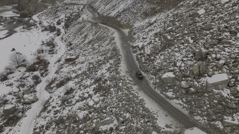Luftaufnahme-Eines-Schwarzen-Lastwagens,-Der-Auf-Der-Straße-Durch-Die-Schneebedeckte-Felslandschaft-Des-Hunza-Tals-Fährt
