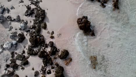 Low-Aerial,-drone-shot-of-a-white-beach-with-rocks-and-small-waves-washing-ashore-at-the-outer-reef-of-the-atoll-of-Fakarava,-French-Polynesia