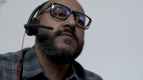 UK-Asian-Male-Talking-On-Headset-Wearing-Glasses-Indoors-Working-From-Home