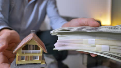Close-up-shot-of-adult-man-lifts-house-or-money-stack-at-home---consideration-of-cash-money-or-estate-investment