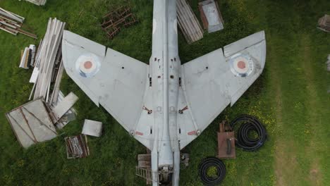 Rising-aerial-view-above-wings-of-distressed-Hawker-hunter-fighter-aircraft-on-British-renovation-farmland-yard
