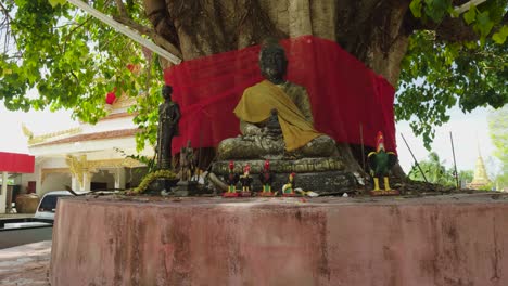 Bodhi-Baum-Mit-Sitzenden-Buddha--Und-Hahnstatuen-Im-Thailändischen-Tempel