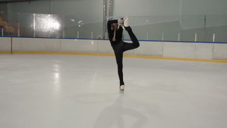 Slow-motion-footage-of-a-young-girl-dressed-in-black-figure-skating-in-an-ice-arena