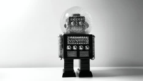 Black-and-white-footage-of-a-robot-snow-globe-on-a-white-desk