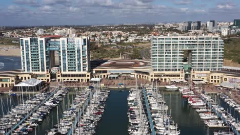 Large-glass-hotels-overlooking-the-long-blue-jetties-with-large-side-yachts-and-motor-boats-moored-in-the-marina-of-Herzliya-in-Israel-on-a-sunny-day