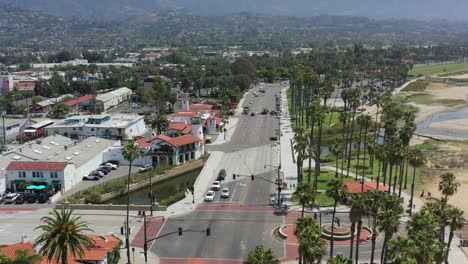aerial-drone-panning-across-a-traffic-light-intersection-as-cars-wait-for-the-light-to-turn-green-in-Santa-Barbara-California-during-a-sunny-summer-day-surrounded-by-tall-palm-trees