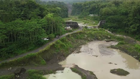 Drone-shot-of-truck-crossing-road-beside-lake-former-sand-mine-in-wilderness-of-Indonesia
